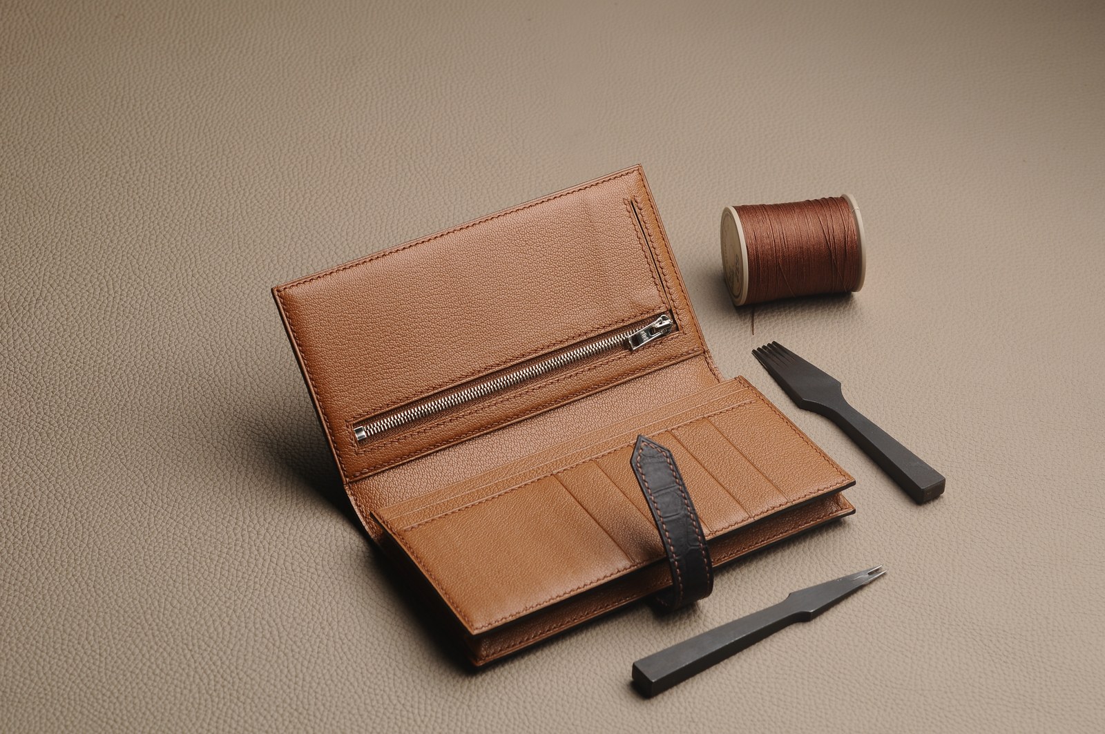 Tan wallet interior with a zip compartment, thread and hand tools