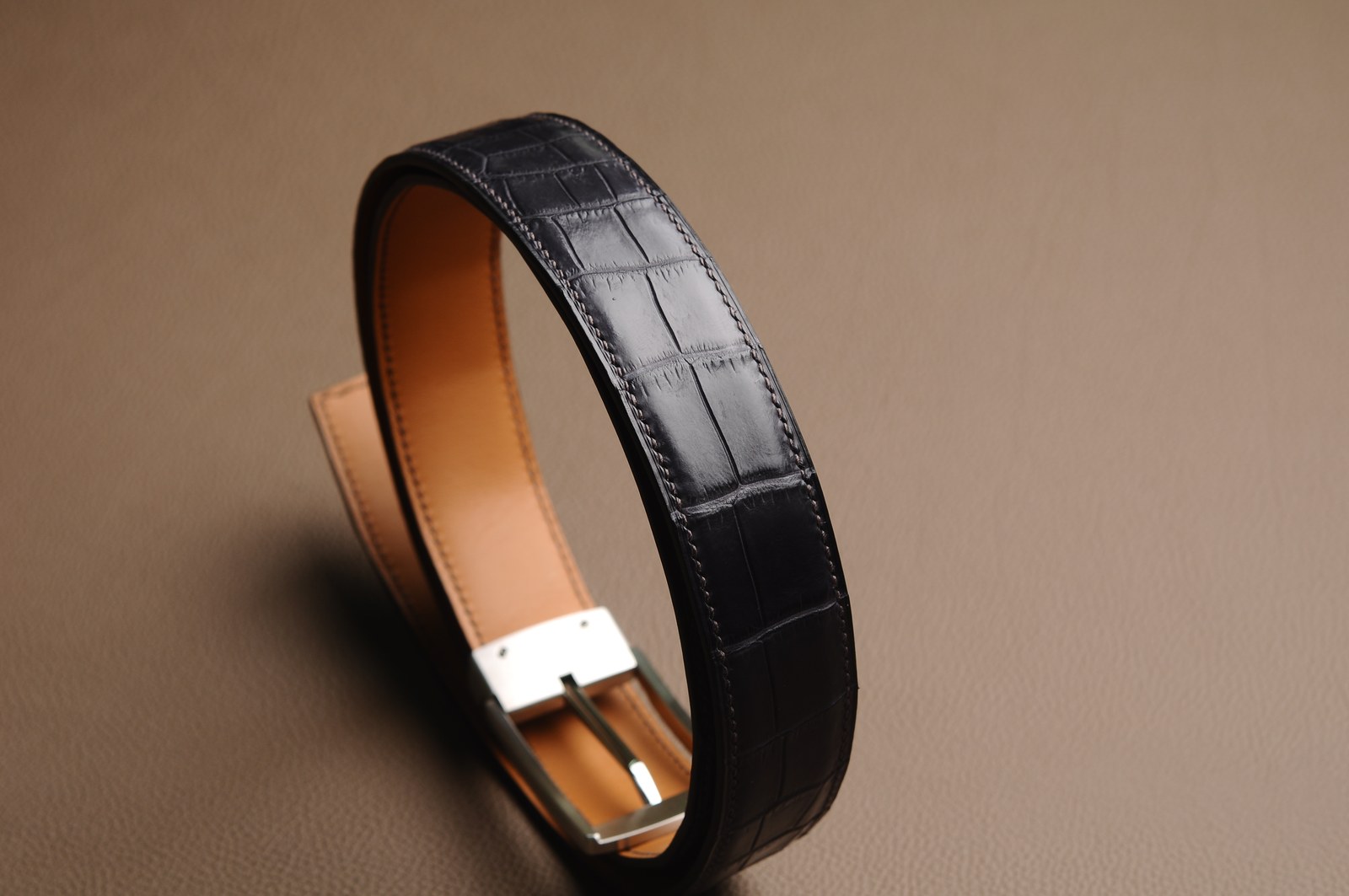 Coiled black crocodile leather belt showing its brown lining and silver hardware