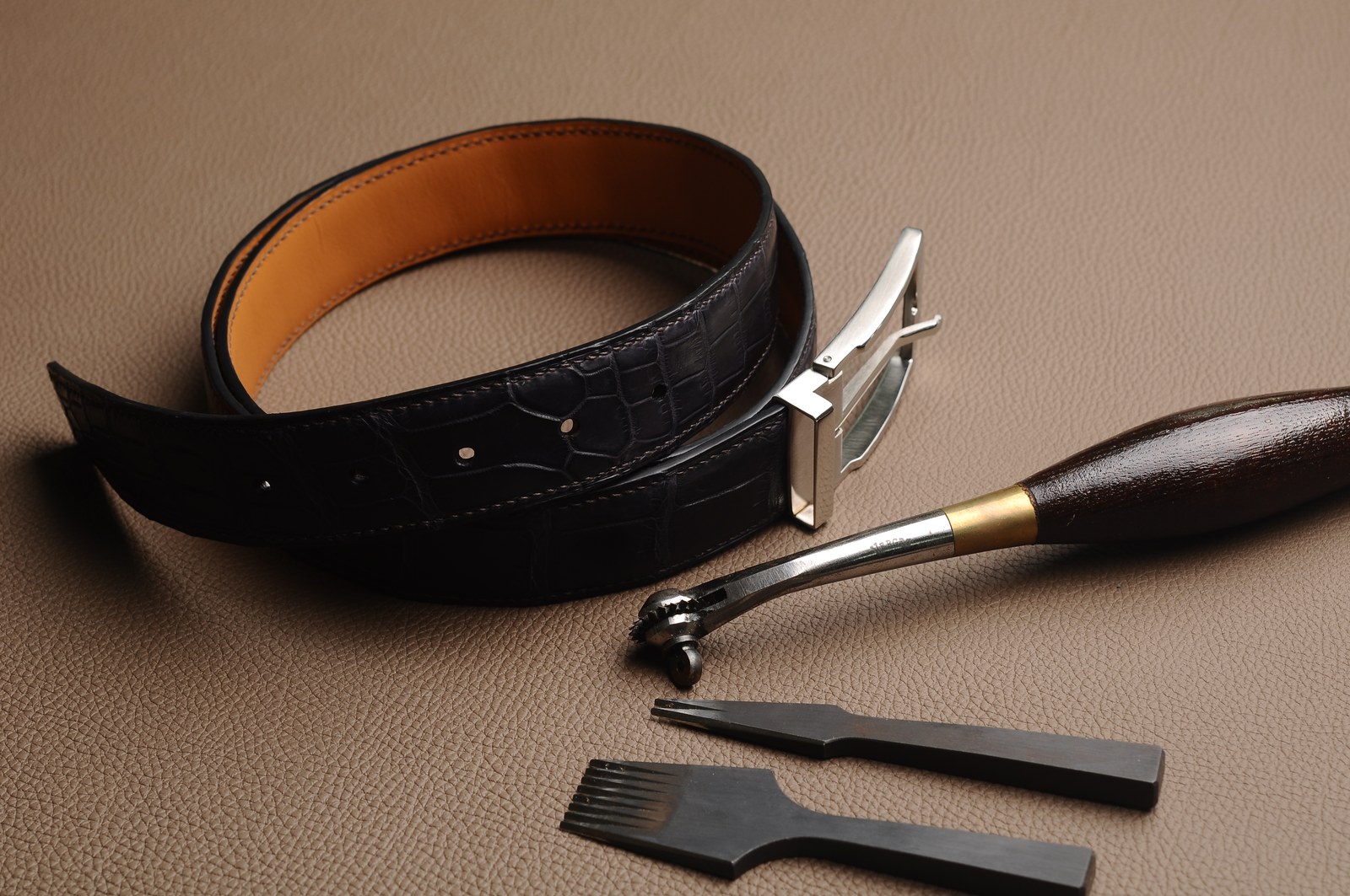 Black leather belt, silver buckle and leatherworking tools arranged together