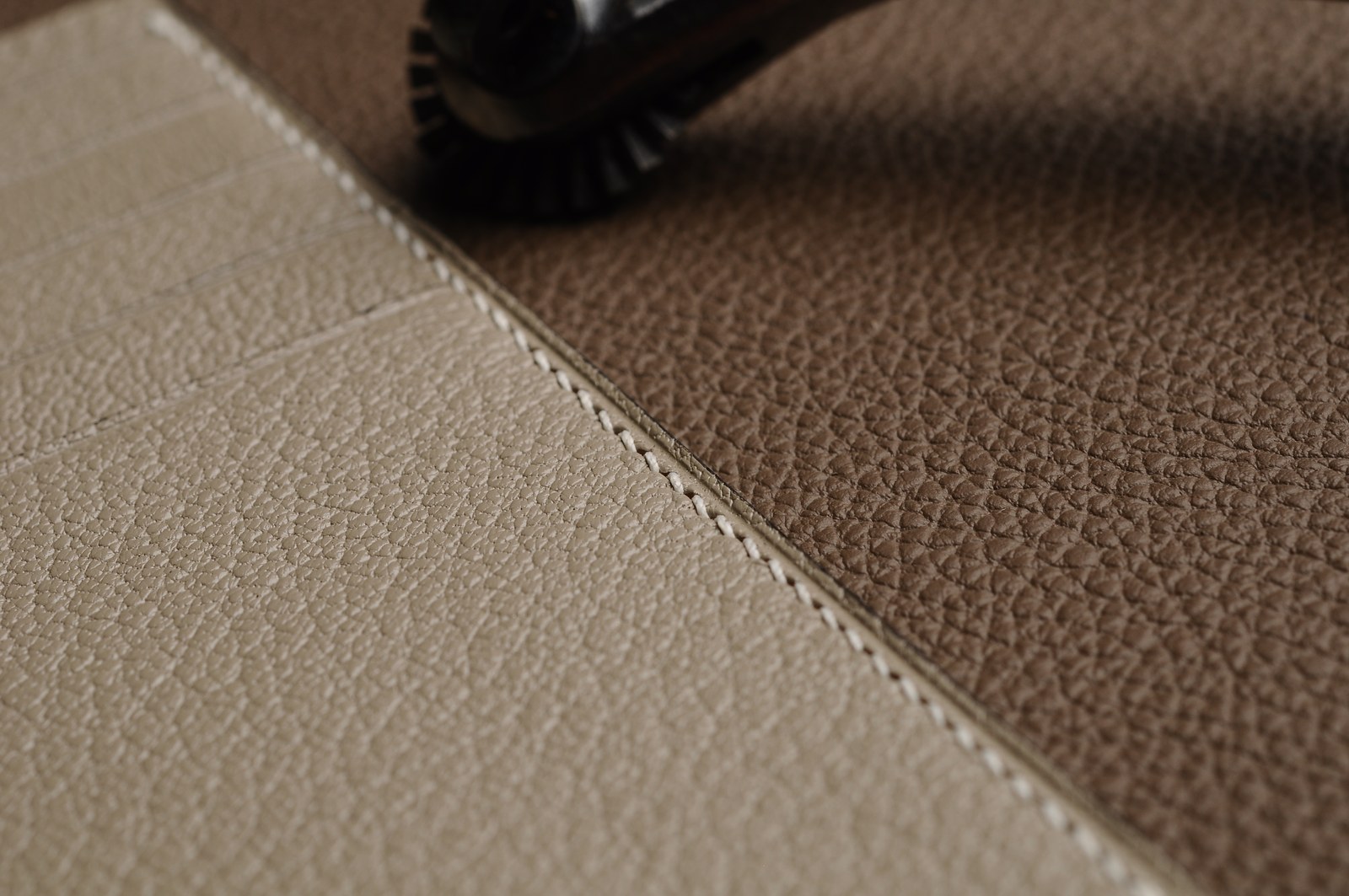 Close-up of a stitched seam joining light and taupe leather panels